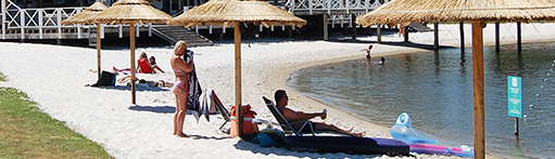 Entspannt chillen am Wasserufer? Mieten Sie für einen ganzen Tag einen Sonnenschirm aus Schilf mit zwei Strandliegen